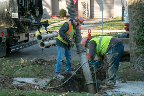 Two construction workers replace a water pipe in a residential neighborhood.